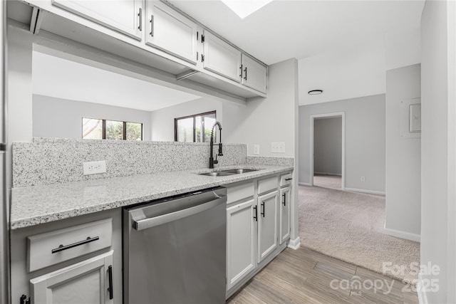 kitchen featuring light stone counters, baseboards, a sink, light carpet, and dishwasher