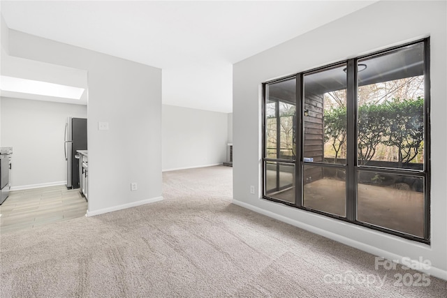 spare room with baseboards, light carpet, and a skylight