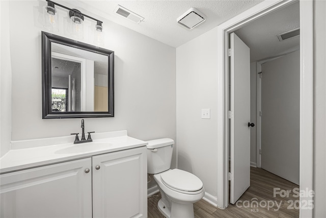 half bath with vanity, wood finished floors, visible vents, a textured ceiling, and toilet