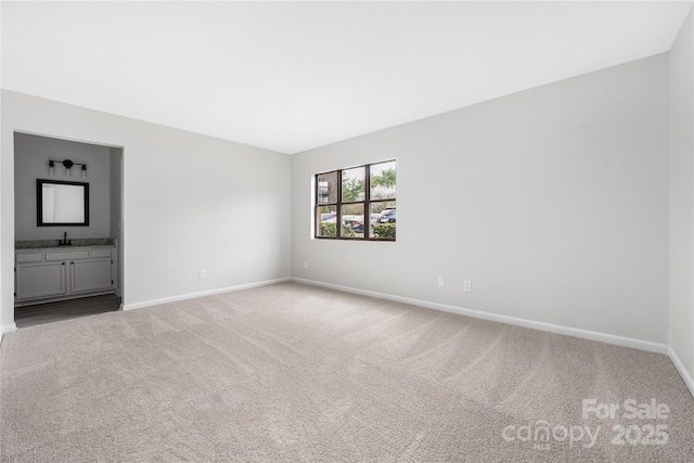 unfurnished bedroom with a sink, baseboards, light colored carpet, and ensuite bathroom