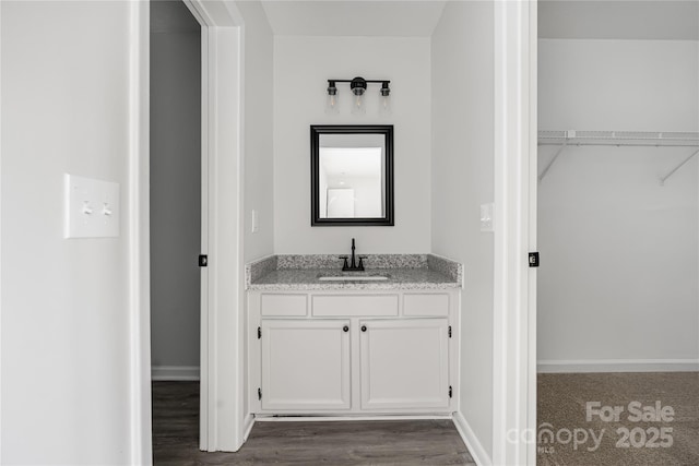 bathroom with a spacious closet, vanity, baseboards, and wood finished floors