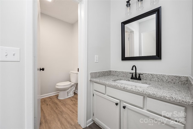 bathroom with vanity, toilet, wood finished floors, and baseboards