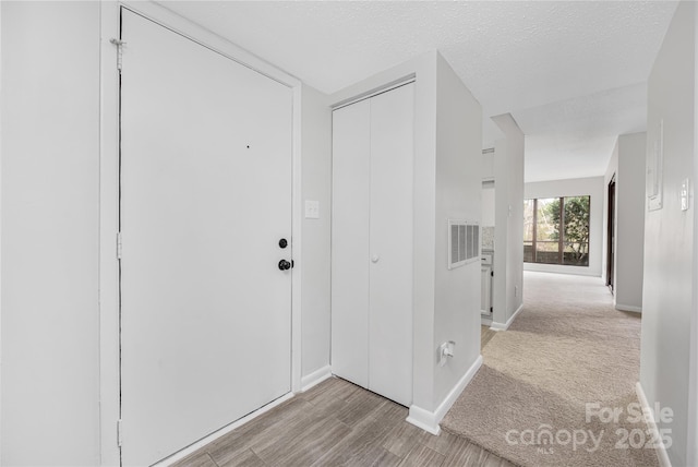 hall with wood finished floors, baseboards, visible vents, and a textured ceiling