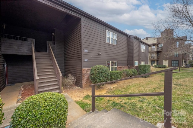 view of property exterior with brick siding, stairs, and a lawn