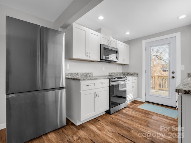 kitchen with stainless steel appliances, wood finished floors, white cabinetry, and light stone countertops