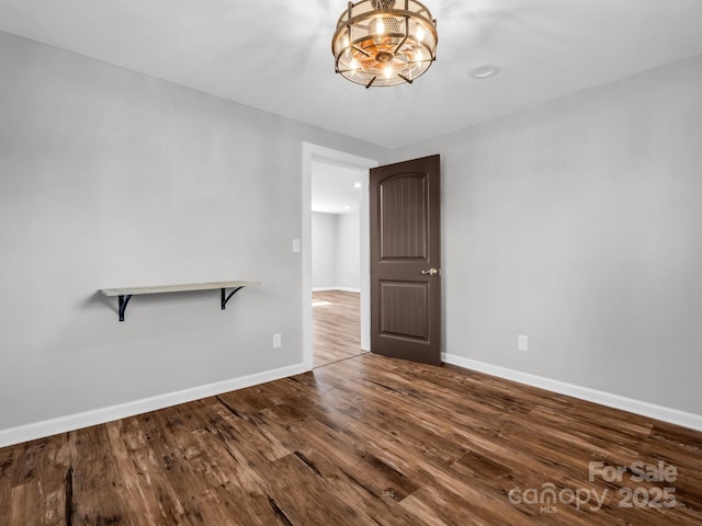 empty room featuring baseboards, a chandelier, and wood finished floors