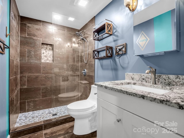 bathroom with tiled shower, vanity, and toilet