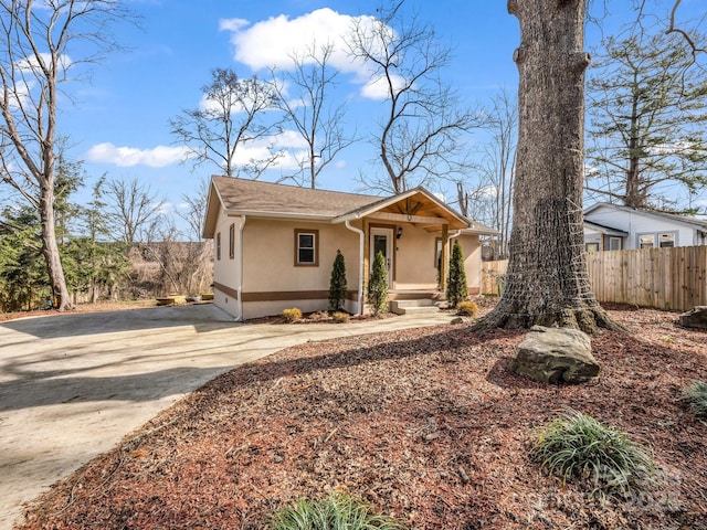 view of front facade featuring driveway, a shingled roof, fence, and stucco siding