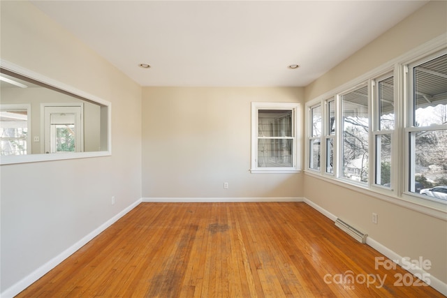 empty room featuring a baseboard heating unit, recessed lighting, wood-type flooring, and baseboards