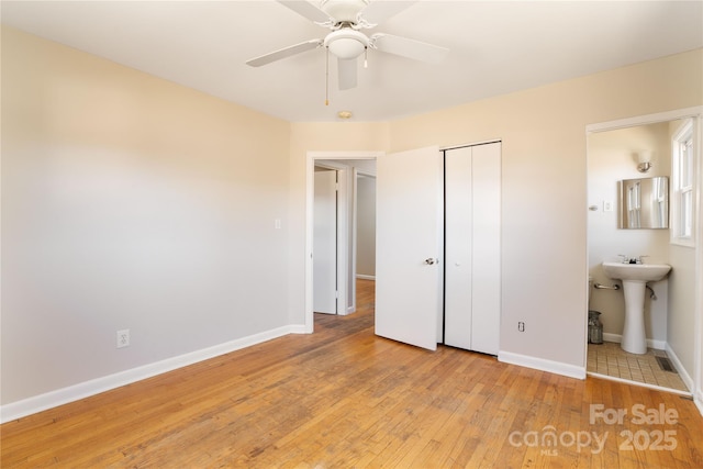 unfurnished bedroom featuring ensuite bathroom, light wood-style flooring, a sink, baseboards, and a closet