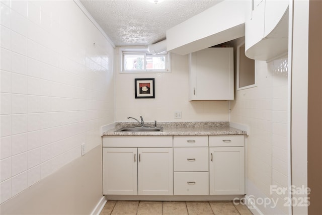 kitchen featuring a textured ceiling, light tile patterned floors, a sink, and tile walls