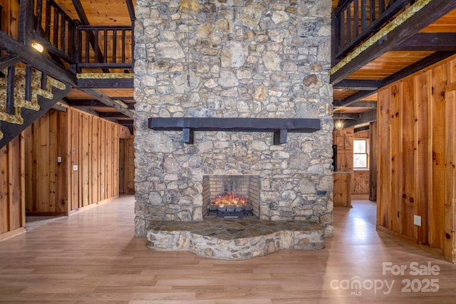 unfurnished living room featuring wood walls, a stone fireplace, a towering ceiling, and wood finished floors