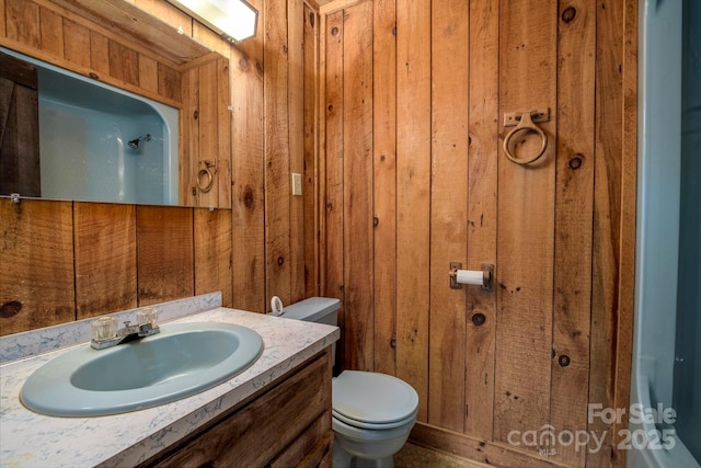 bathroom with a closet, vanity, toilet, and wooden walls