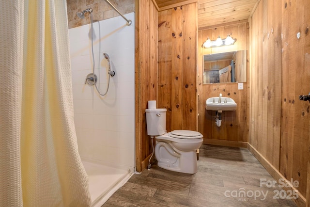 bathroom featuring toilet, a stall shower, wood walls, wood finished floors, and baseboards