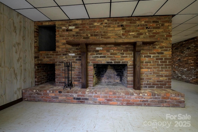 interior details with a paneled ceiling, a brick fireplace, wooden walls, and baseboards