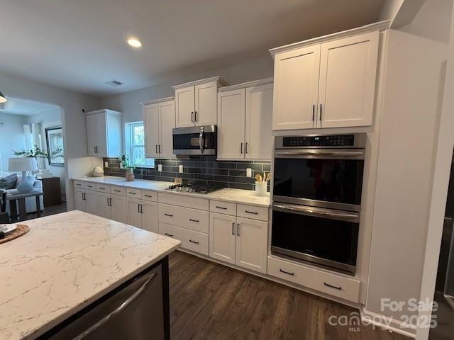 kitchen with light stone countertops, stainless steel appliances, white cabinets, decorative backsplash, and dark wood-style floors