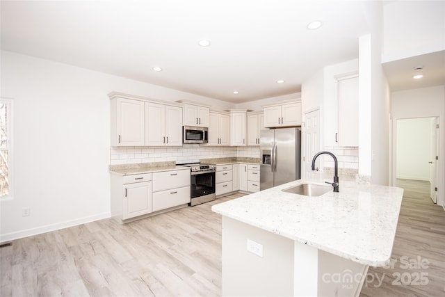 kitchen featuring stainless steel appliances, light wood-style floors, a sink, and a peninsula