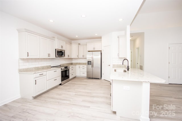 kitchen with stainless steel appliances, a peninsula, a sink, and light wood-style floors