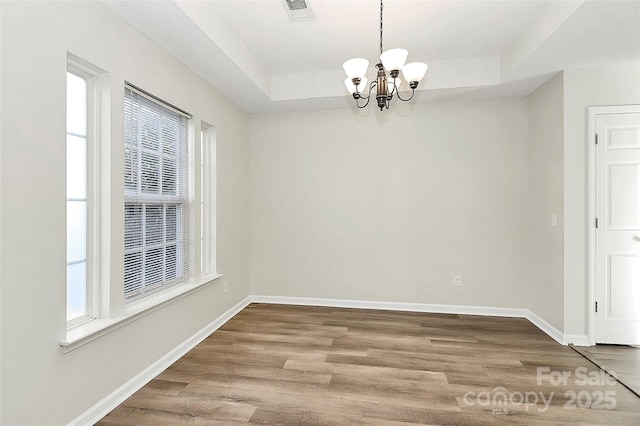 unfurnished dining area with wood-type flooring, a tray ceiling, and a notable chandelier