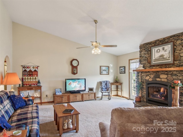 carpeted living room featuring ceiling fan, vaulted ceiling, and a stone fireplace