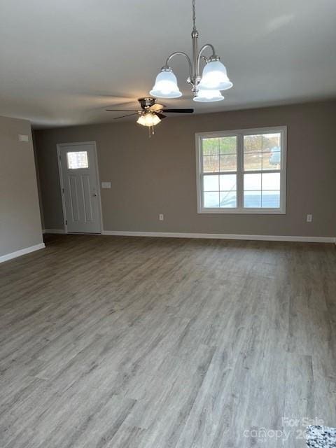 interior space with ceiling fan with notable chandelier, wood finished floors, and baseboards