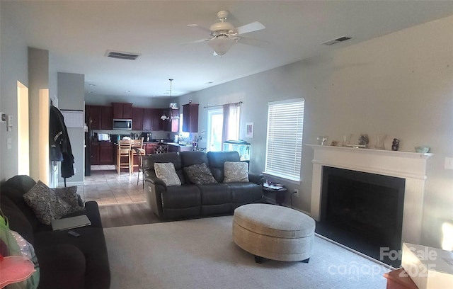 living area with ceiling fan, a fireplace with flush hearth, and visible vents