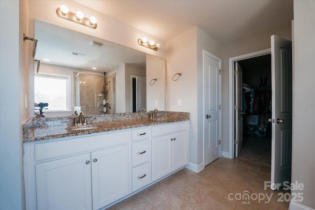 bathroom featuring double vanity, a spacious closet, a stall shower, and a sink