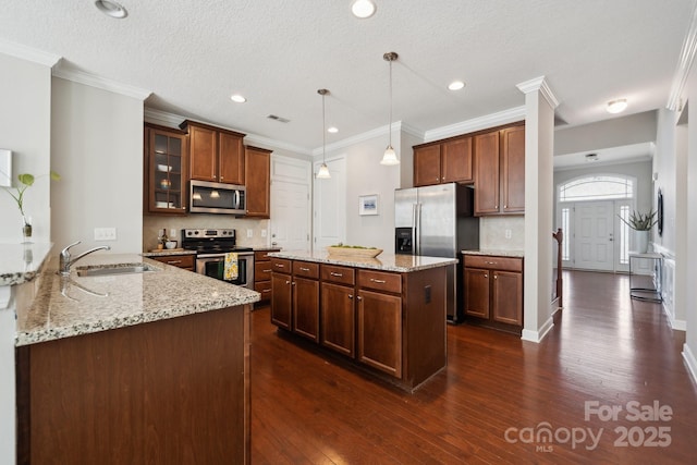 kitchen with light stone counters, a sink, appliances with stainless steel finishes, dark wood finished floors, and glass insert cabinets