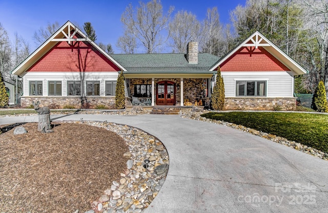 craftsman-style home featuring stone siding, french doors, driveway, and a chimney