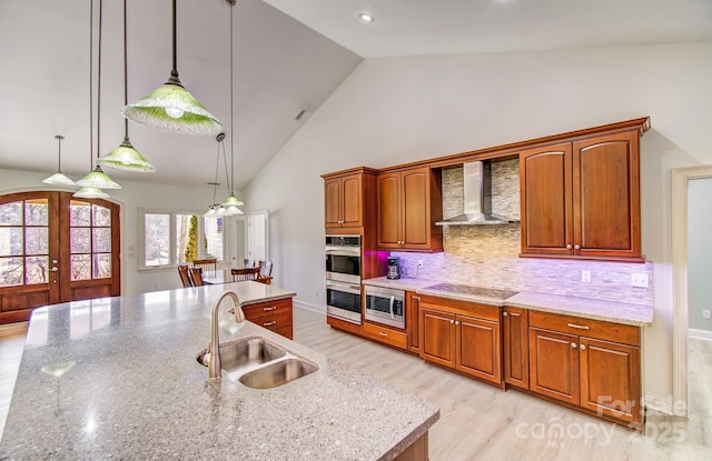 kitchen with pendant lighting, a center island with sink, stainless steel appliances, a sink, and wall chimney range hood