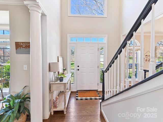 entrance foyer with dark wood-type flooring, plenty of natural light, stairway, and decorative columns