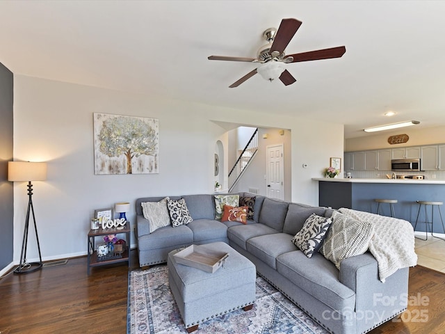 living room featuring baseboards, visible vents, ceiling fan, dark wood-type flooring, and stairs