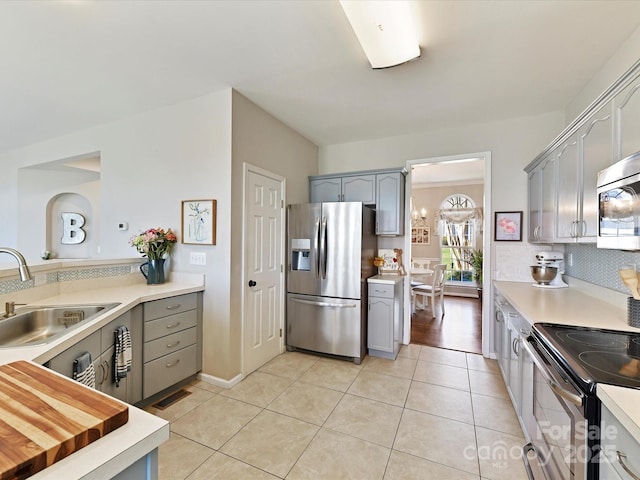 kitchen with stainless steel appliances, a sink, gray cabinetry, and light tile patterned floors