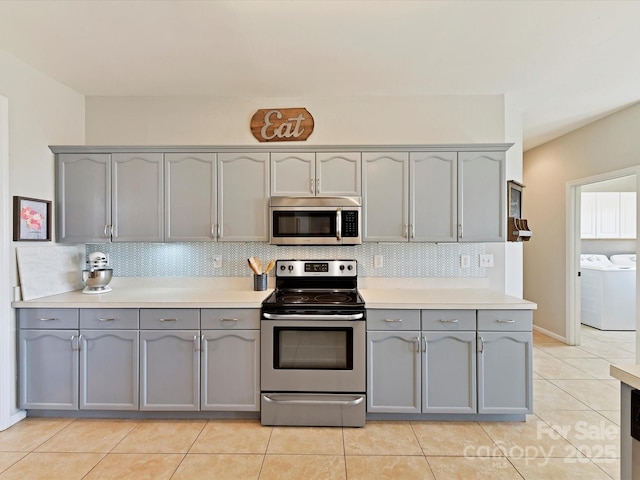 kitchen with tasteful backsplash, appliances with stainless steel finishes, washing machine and clothes dryer, light countertops, and gray cabinetry