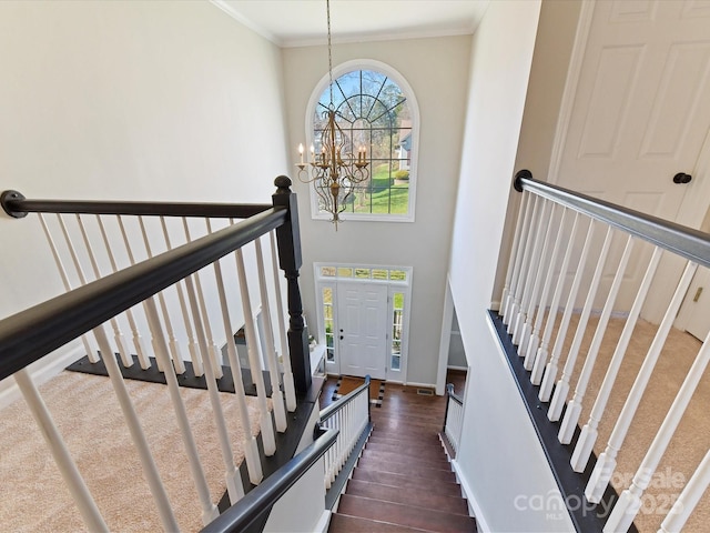 staircase featuring a high ceiling, wood finished floors, baseboards, ornamental molding, and an inviting chandelier