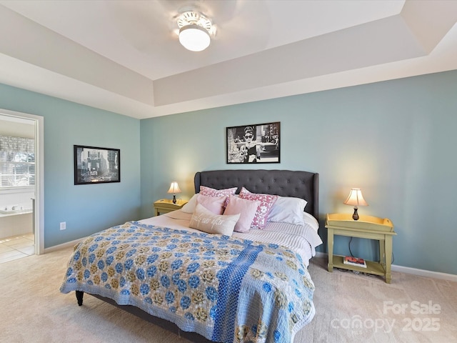 carpeted bedroom with ensuite bathroom, a tray ceiling, a ceiling fan, and baseboards