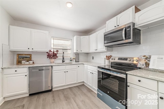 kitchen with stainless steel appliances, a sink, white cabinetry, and light stone countertops