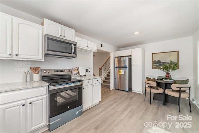 kitchen with appliances with stainless steel finishes, light wood-type flooring, backsplash, and white cabinets