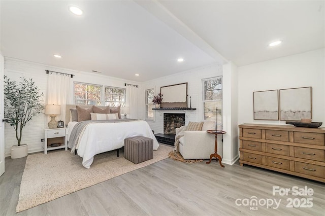 bedroom featuring a brick fireplace, light wood-style flooring, and recessed lighting