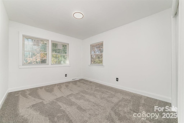 empty room with carpet, visible vents, and baseboards