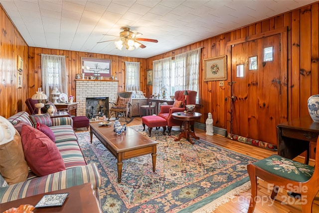 living room featuring wooden walls, a fireplace, a ceiling fan, and wood finished floors