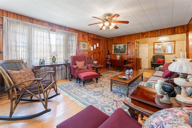 living room with ceiling fan, wood-type flooring, and wooden walls