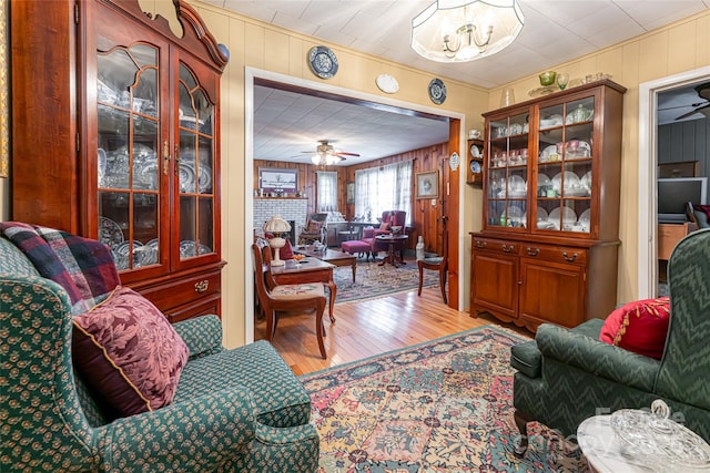 living room with ceiling fan with notable chandelier, a fireplace, wood finished floors, and wooden walls