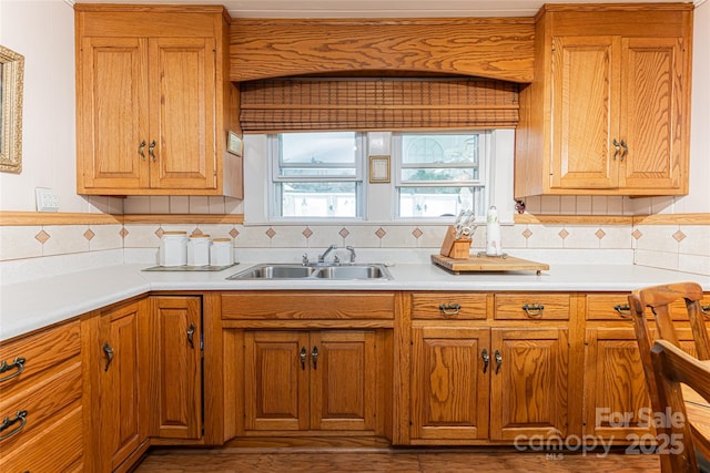 kitchen with brown cabinets, light countertops, a sink, and decorative backsplash