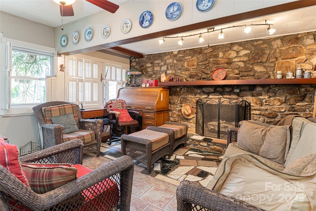 living area with ceiling fan, a fireplace, stone finish floor, and beamed ceiling