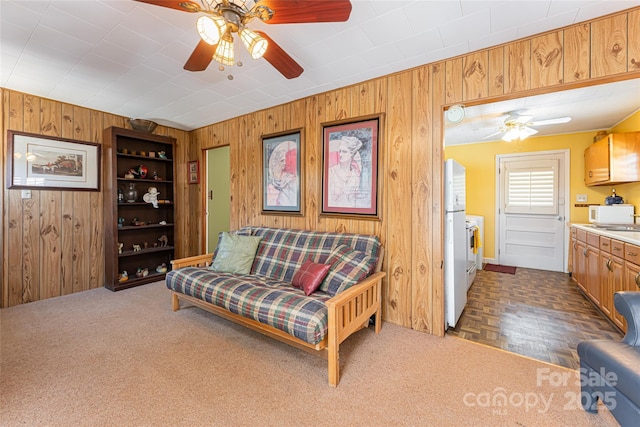 living area with ceiling fan and wooden walls