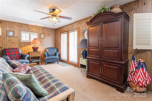 living room featuring a ceiling fan, light carpet, and wood walls