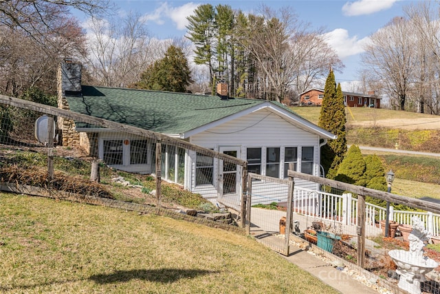 rear view of house featuring a yard, a chimney, and roof with shingles