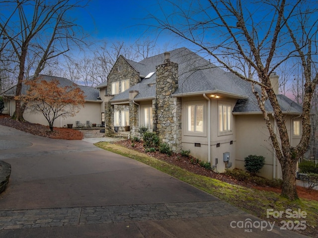 view of front of house with a chimney, stucco siding, a shingled roof, stone siding, and driveway