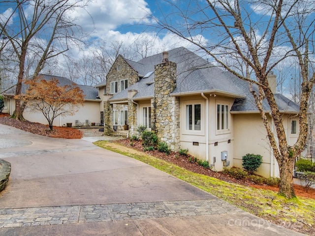 view of front of house featuring a chimney, stucco siding, a shingled roof, stone siding, and driveway